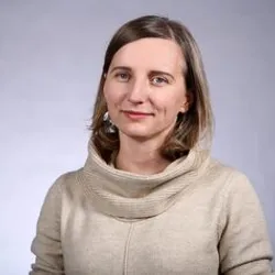Monika Piotrowska, a bioethicist, wears a cream-colored sweater against a grey background.