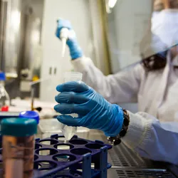 A person wearing a white lab coat carrying out cancer research in a lab.