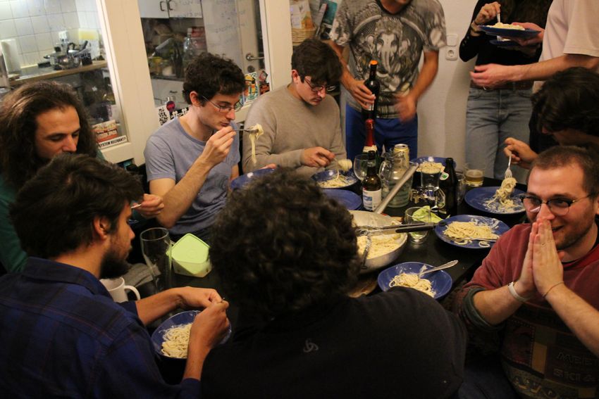 A group of people sit together eating bowls of pasta. A group of people sit together eating bowls of pasta.