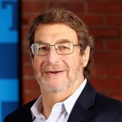 Fred D. Ledley wears glasses and a dark suit jacket in a headshot photo against a brick wall.