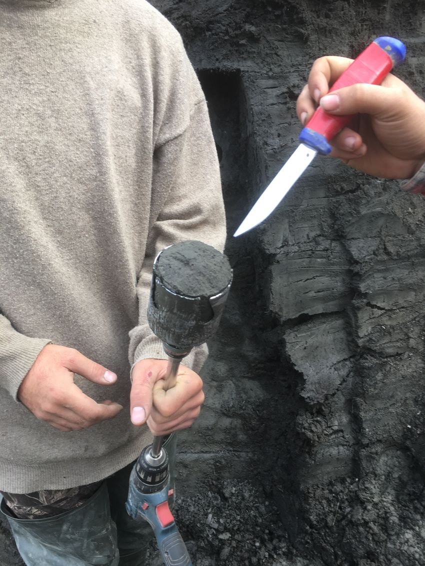A man holds a core drilled from the permafrost, which a scientist is pointing to with a knife.