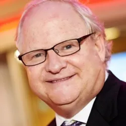 Carl Kurlander wears black glasses and a dark suit in a headshot photo.