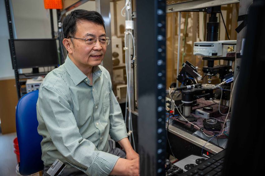 Ru-Rong Ji, wearing a striped shirt and glasses, sits by a microscope in a laboratory. Ru-Rong Ji, wearing a striped shirt and glasses, sits by a microscope in a laboratory.