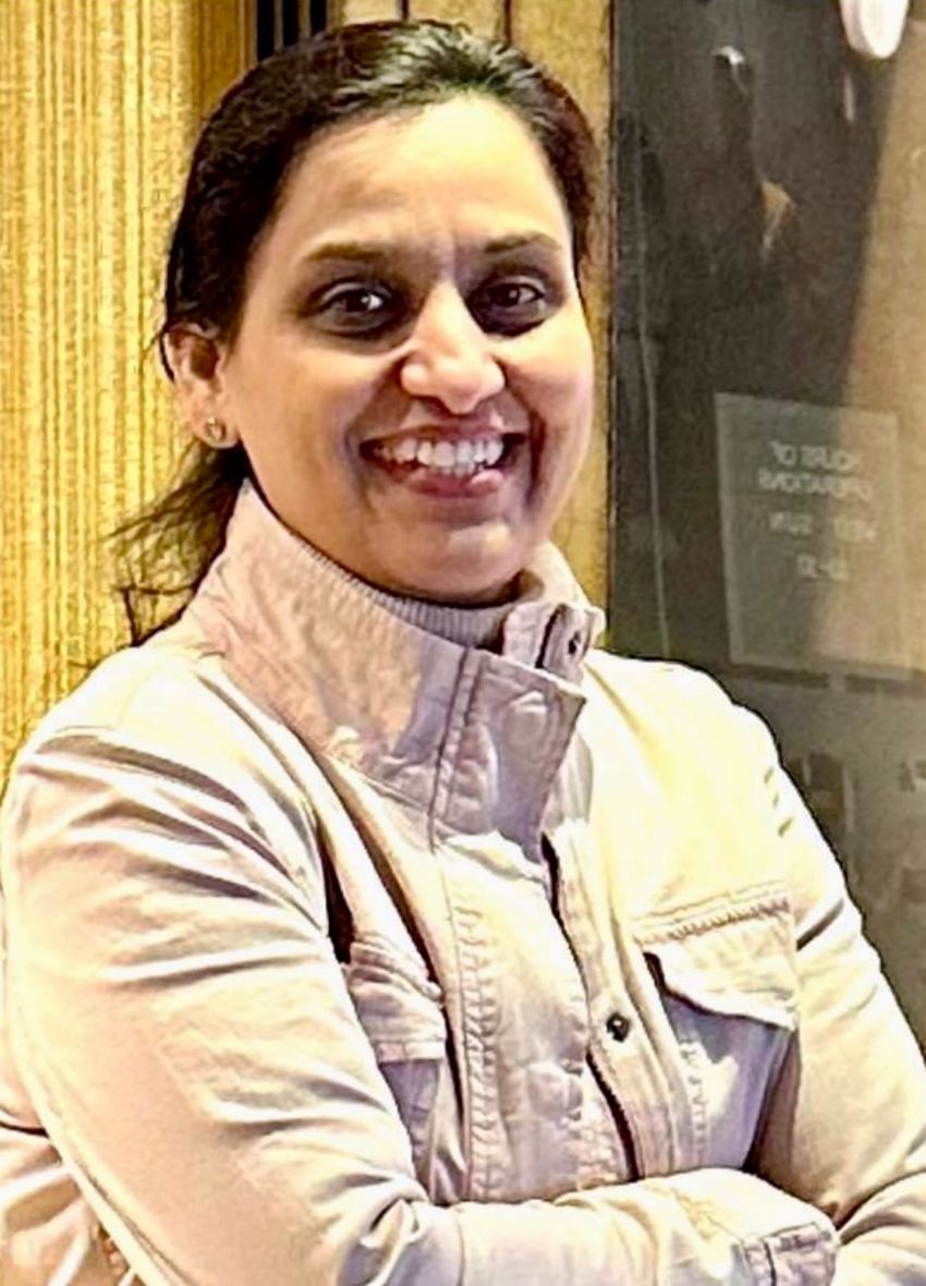 Priya Bhardwaj smiles while wearing a white jacket with her arms crossed.