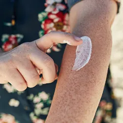 Image of a person applying sunscreen to their freckled arm.