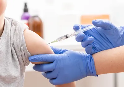 A young boy gets a vaccine in his arm from a doctor wearing blue gloves.