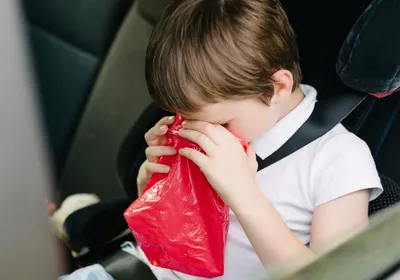 A child vomiting in a car, presumably suffering from motion sickness.