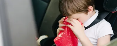 A child vomiting in a car, presumably suffering from motion sickness.