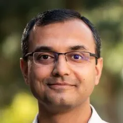 Two employees sit at a desk working on laptops with an AI robot. They have conversation bubbles above them.