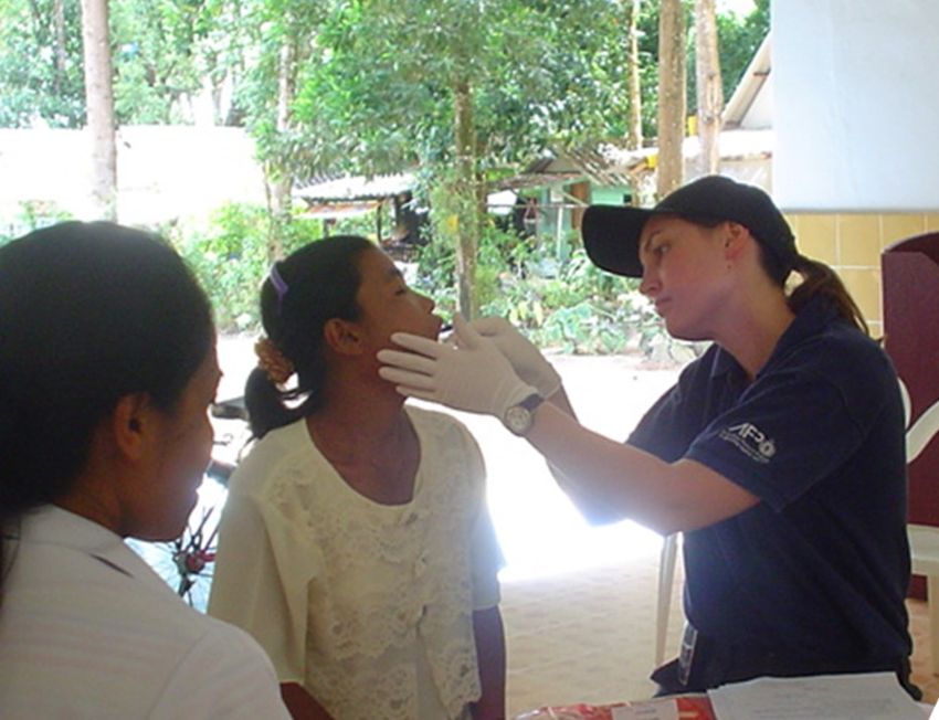 Forensic biologist Kirsty Wright is collecting a buccal swab from a woman for DNA analysis in Thailand after the 2004 Boxing Day Tsunami. She is wearing a dark shirt and cap, and white gloves.