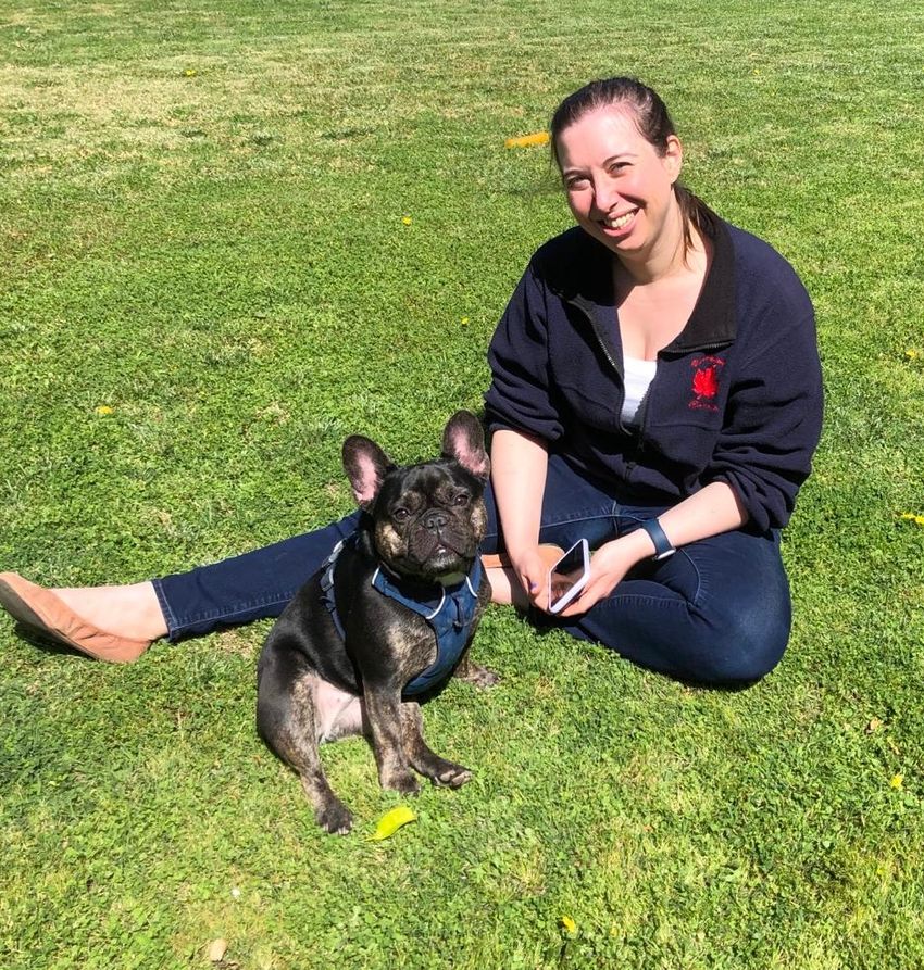 Image of Stephanie DeMarco sitting in a grassy yard next to a small black dog.