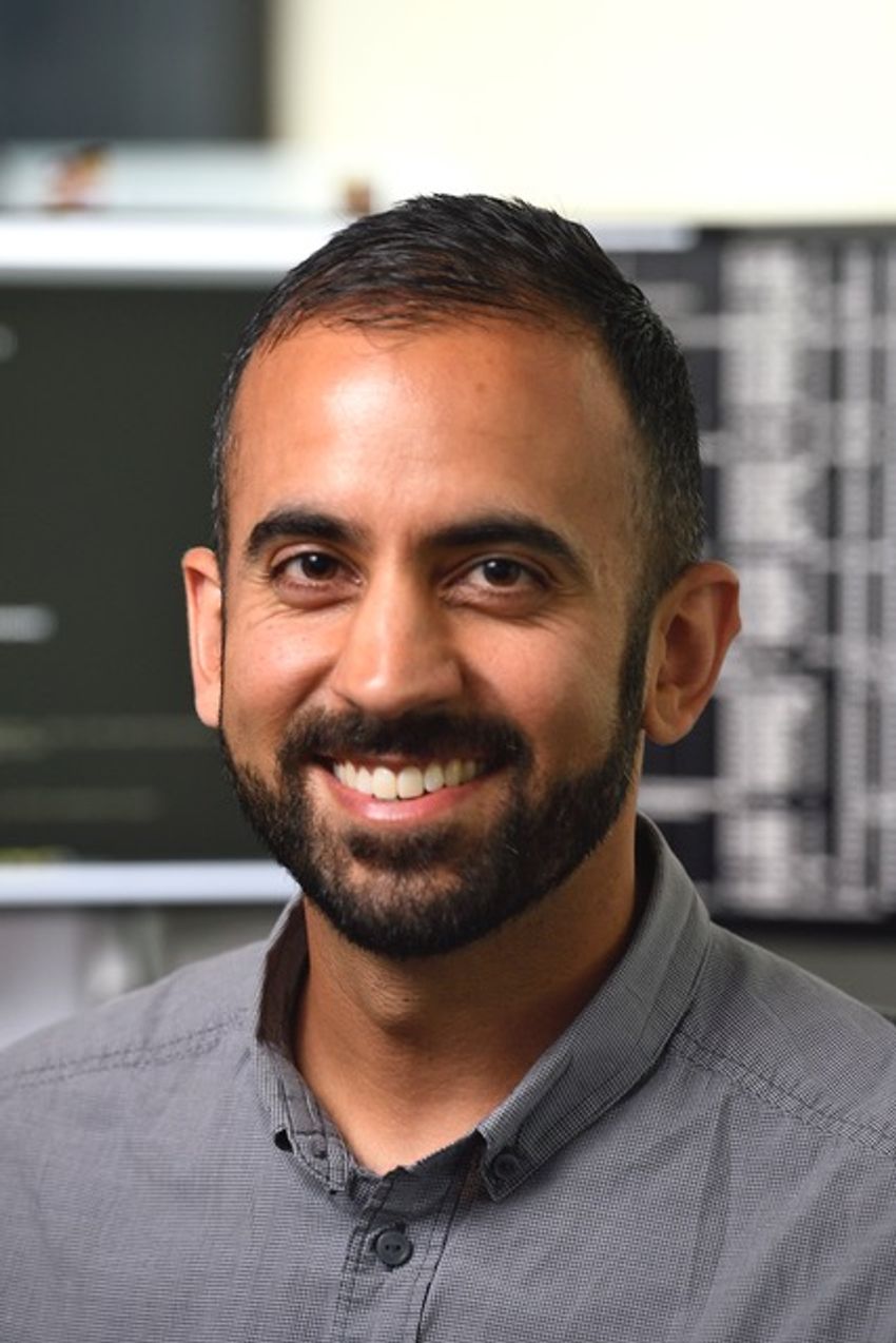 Rajiv McCoy, wearing a gray button-up shirt, smiles at the camera.