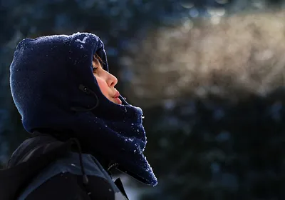 A young boy wrapped up in a winter jacket breathes out, forming a cloud of air.