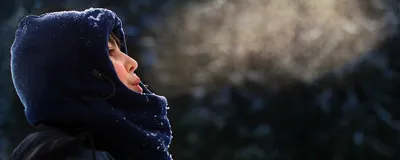 A young boy wrapped up in a winter jacket breathes out, forming a cloud of air. A young boy wrapped up in a winter jacket breathes out, forming a cloud of air.
