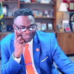 Andre Hudson, PhD wears a blue suit jacket, an orange tie, and glasses in a lab office.