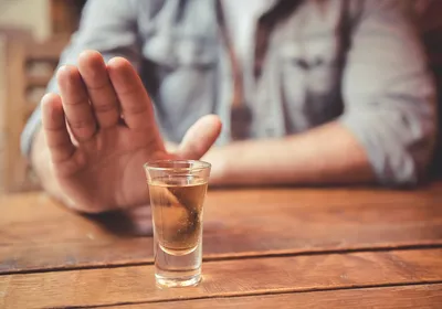 A man holds out his hand refusing an alcoholic drink.