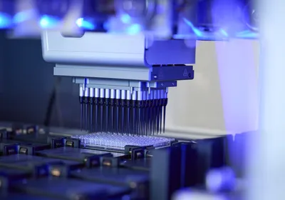 Photo of an automated liquid handling device pipetting liquid into a multi-well plate.