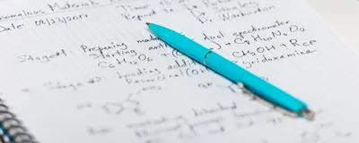 A blue pen sits on top of a notebook with writing in it.