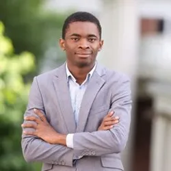 Kwesi Akonu Adom Mensah Forson wears a grey suit jacket while crossing his arms in a photo outside.