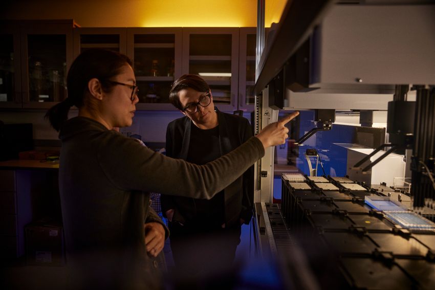 Image of study coauthors Michelle Tang (left) and Aimée Dudley (right) stand next to a machine that processes genetic samples.