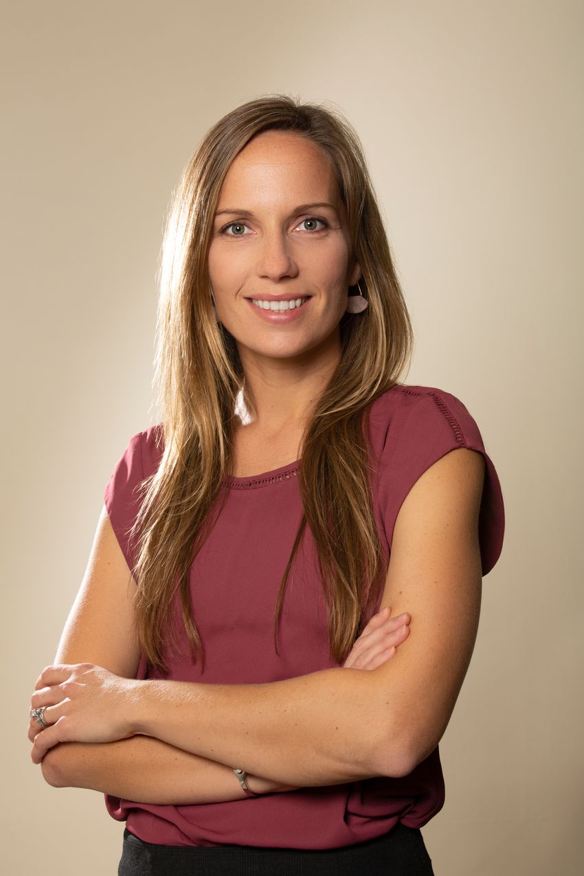 A photograph of Deirdre Tobias, an epidemiologist at Brigham and Women’s Hospital and Harvard University. Tobias is standing in front of a beige background and is smiling at the camera with her arms loosely crossed. She has long, brown hair and is wearing a maroon shirt.