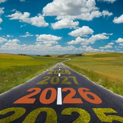 Image of a road cutting through a field under a blue sky with clouds. On the road, the years “2025”, “2026”, “2027”, “2028” are painted leading down the road. 2026 is in orange. This represents the outlook for research in 2026. 