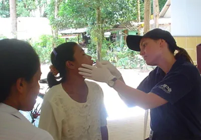 Forensic biologist Kirsty Wright is collecting a buccal swab from a woman for DNA analysis in Thailand after the 2004 Boxing Day Tsunami. She is wearing a dark shirt and cap, and white gloves.