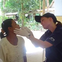 Forensic biologist Kirsty Wright is collecting a buccal swab from a woman for DNA analysis in Thailand after the 2004 Boxing Day Tsunami. She is wearing a dark shirt and cap, and white gloves.