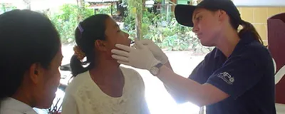 Forensic biologist Kirsty Wright is collecting a buccal swab from a woman for DNA analysis in Thailand after the 2004 Boxing Day Tsunami. She is wearing a dark shirt and cap, and white gloves.