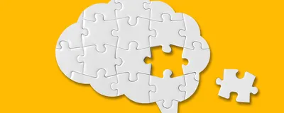 Photograph of a white puzzle in the shape of a brain on a yellow background. One puzzle piece from the center of the brain is missing. This photo represents a word losing its meaning in a phenomenon called semantic satiation. 