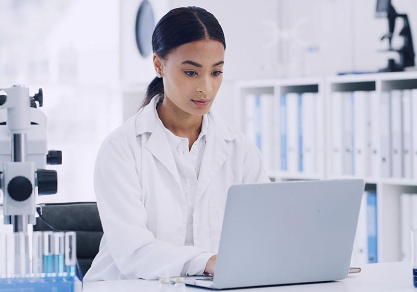 A photo of a scientist in the laboratory typing on her laptop