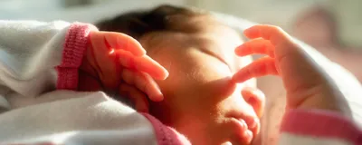 A newborn baby sleeps while touching her face.