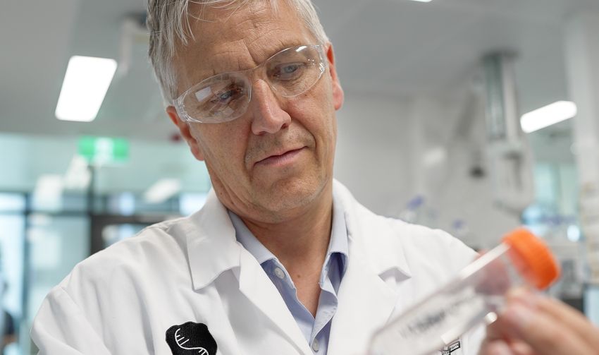 Pall Thordarson wears a white lab coat and safety glasses, and holds an orange-lidded flask.