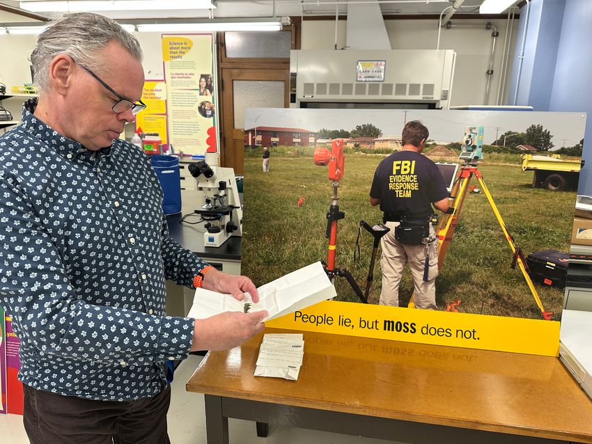 von Konrat with the moss specimens used in the Burr Oak case. In the background is a panel from the Field Museum’s 2017 exhibition, Specimens, which highlighted the Burr Oak case as an example of how museum specimens are used. This panel contains a photograph of an FBI worker at the scene and the text “People lie, but moss does not.”