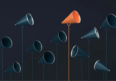 Ten dark blue megaphones and one orange megaphone stand pointing in different directions and at different heights against a dark background. The orange megaphone stands out because of its different color and it is one of the tallest megaphones.