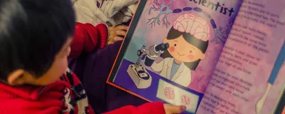 A young child holding one of the CuSTEMized books that is open to a page titled ‘N is for Neuroscientist.’