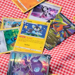 Photograph of different Pokémon cards spread disorderly out over a red and white checked blanket.