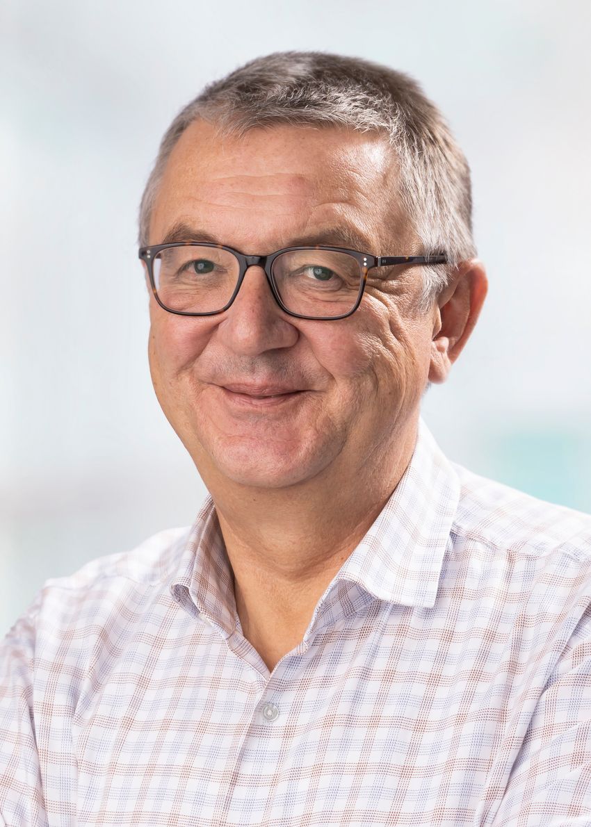 Ralf Reski is smiling, wearing dark-rimmed glasses and a pale checked shirt on a white background.