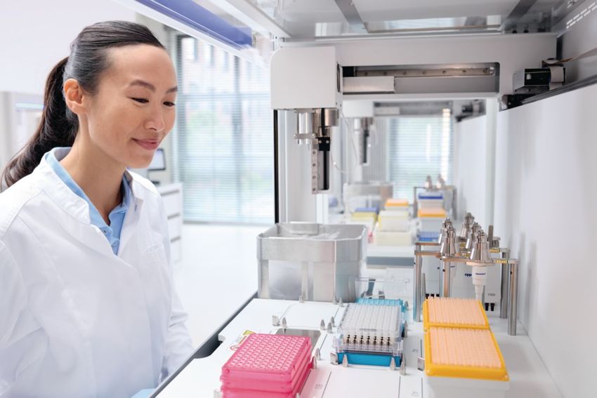 Image of a smiling scientist in a lab coat gazing at pipette tips and an automated pipette on a workbench. Image of a smiling scientist in a lab coat gazing at pipette tips and an automated pipette on a workbench.