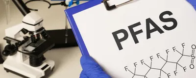 A researcher holding a clipboard with a sheet of paper that reads PFAS and includes a PFAS chemical structure