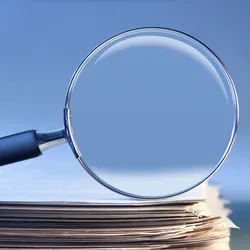 A magnifying glass rests on top of a stack of paper.