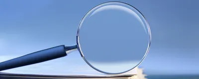 A magnifying glass rests on top of a stack of paper.