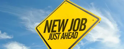 Photo of a bright yellow, diamond-shaped road sign with the words “New Job Just Ahead” printed in black. 
