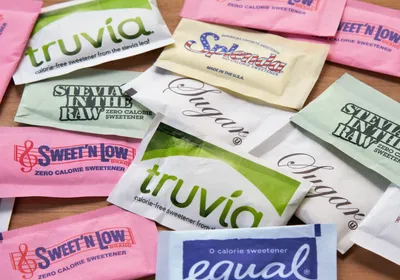 Image of various packets of both artificial and natural sweeteners on a table.