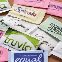Image of various packets of both artificial and natural sweeteners on a table.