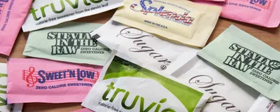 Image of various packets of both artificial and natural sweeteners on a table.