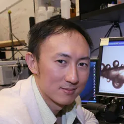 David Hu wears a light-colored shirt in front of a computer in a laboratory space.