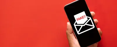 A hand holds a smartphone that shows an email icon with the word “fake” on it.