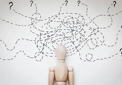 Cartoon of a wooden human-shaped figure against a white wall with several overlapping and tangled dotted lines above their head. The dashed lines end in question marks at the edge of the image. 