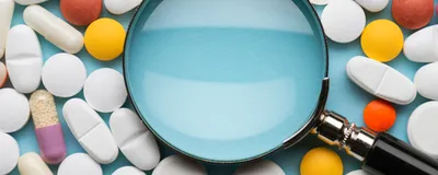Image of various pills surrounding a magnifying glass